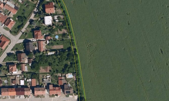 Žlutě je vyznačen obecní pozemek kolem obytné zástavby. Zelená čára je hranice pšeničného pole, na kterém jsou vidět vyježděné koleje od postřikovače. Na obecním pozemku je vidět vzrostlá dřevitá vegetace, která odděluje zahrady od pole. Přesto lze v některých úsecích toto nárazníkové pásmo ještě rozšířit. Zdroj: LPIS, Živá půda